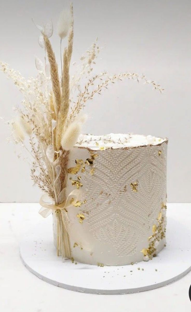 a white cake with gold sprinkles sits on a plate next to some dried flowers