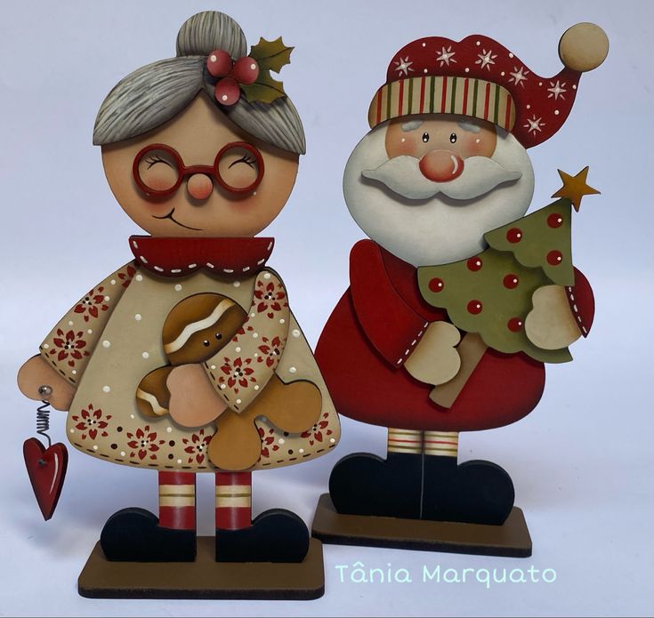 two wooden christmas figurines with santa and mrs claus holding a tree, one is holding a teddy bear