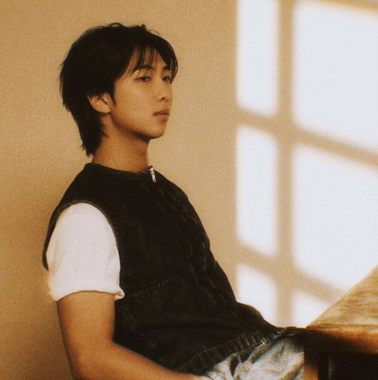 a young man sitting at a wooden table in front of a window with sunlight streaming through it