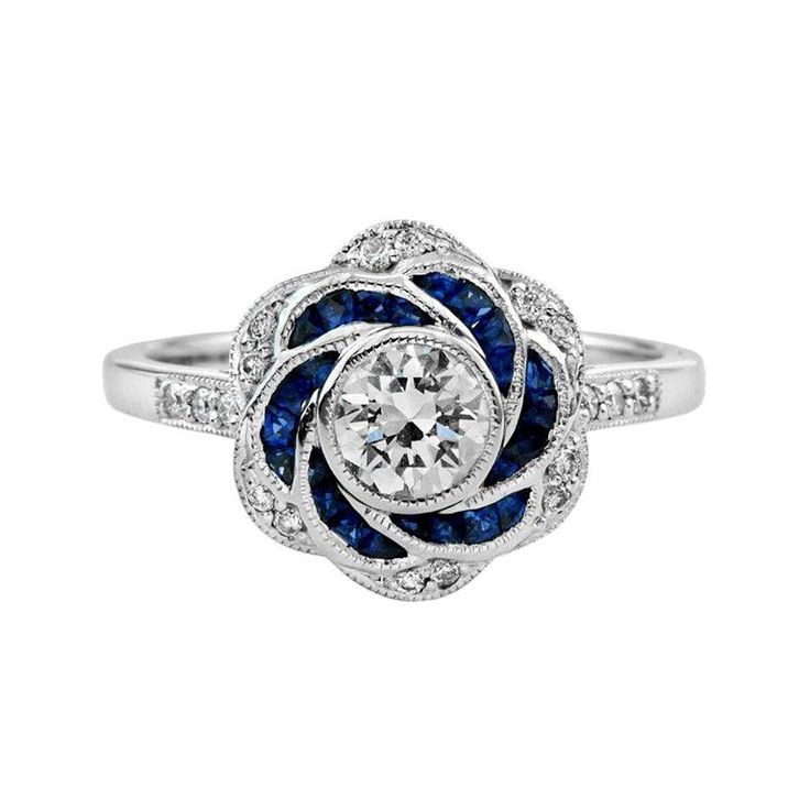 Artistry and sophistication come together in a flower ring with sapphires and diamonds from the Art Deco era. The ring features a round shape center which you can place any round diamond on it in a bezel setting surrounded by French French Cut Color Stones (you can select Blue Sapphire, Emerald, Ruby), round brilliant diamonds on shoulders add the sparkle to this beautiful ring. Ring Information Style: Art-deco Metal: 18K White Gold Weight: 4.35 g. (approx. total weight) Center Gemstones Type: D Art Deco Engagement Ring Sapphire, Engagement Rings With Sapphires, Vintage Wedding Rings Antique, Vintage Sapphire Engagement Rings, Diamond And Sapphire Engagement Ring, Blue Sapphire Wedding Ring, Blue Wedding Rings, Art Deco Jewelry Vintage, Blue Sapphire Engagement Ring