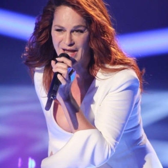 a woman holding a microphone in her right hand and wearing a white dress on stage