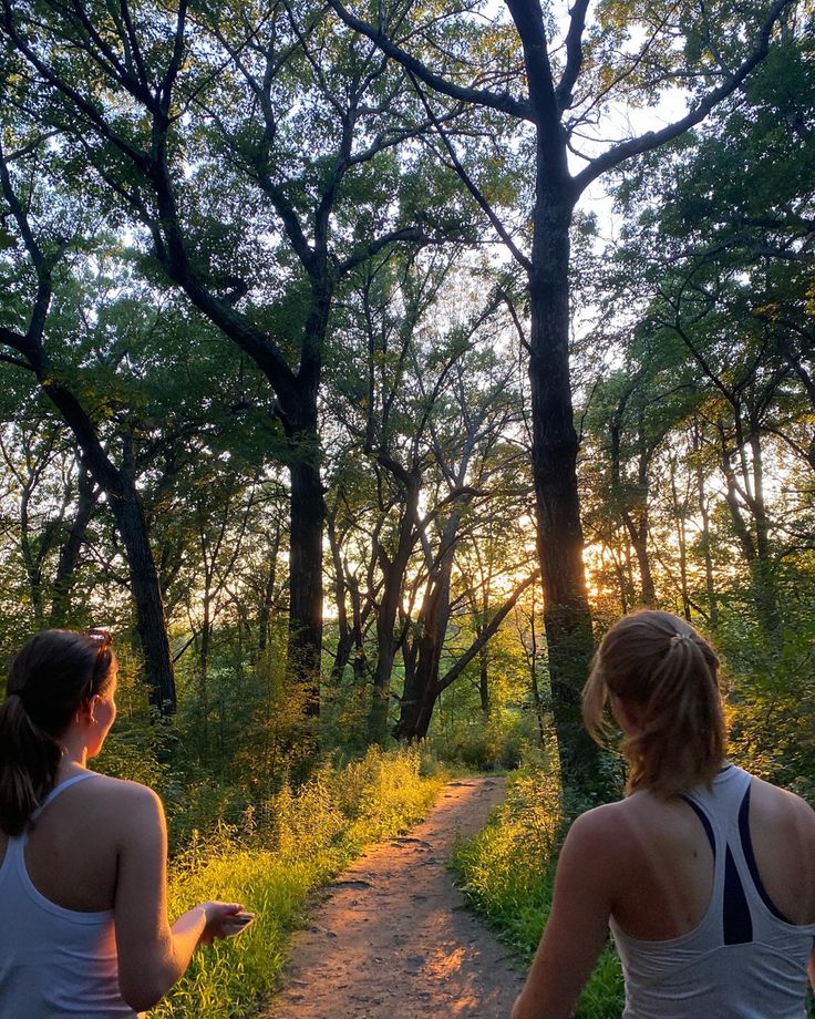 two women are walking down a path in the woods