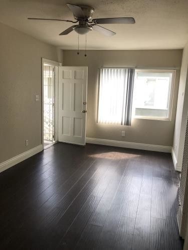 an empty room with hard wood floors and a ceiling fan in the corner between two windows