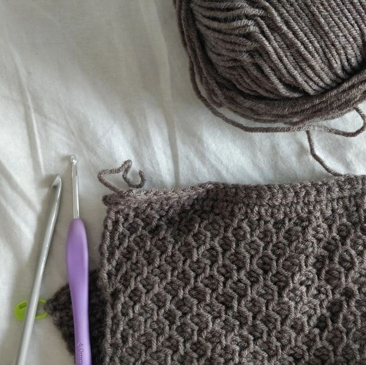 two crocheted knitting needles next to a gray knitted bag and ball of yarn