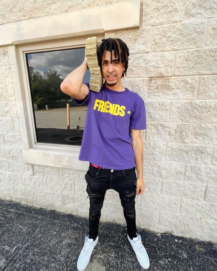 a young man with dreadlocks and a purple shirt is standing in front of a window