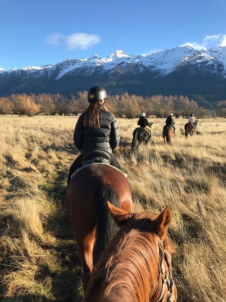 several people riding horses on a grassy field with mountains in the background and snow - capped peaks