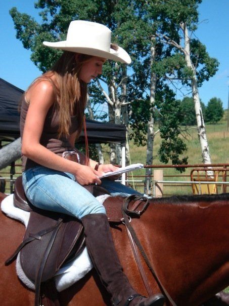 a woman in cowboy hat sitting on top of a brown horse