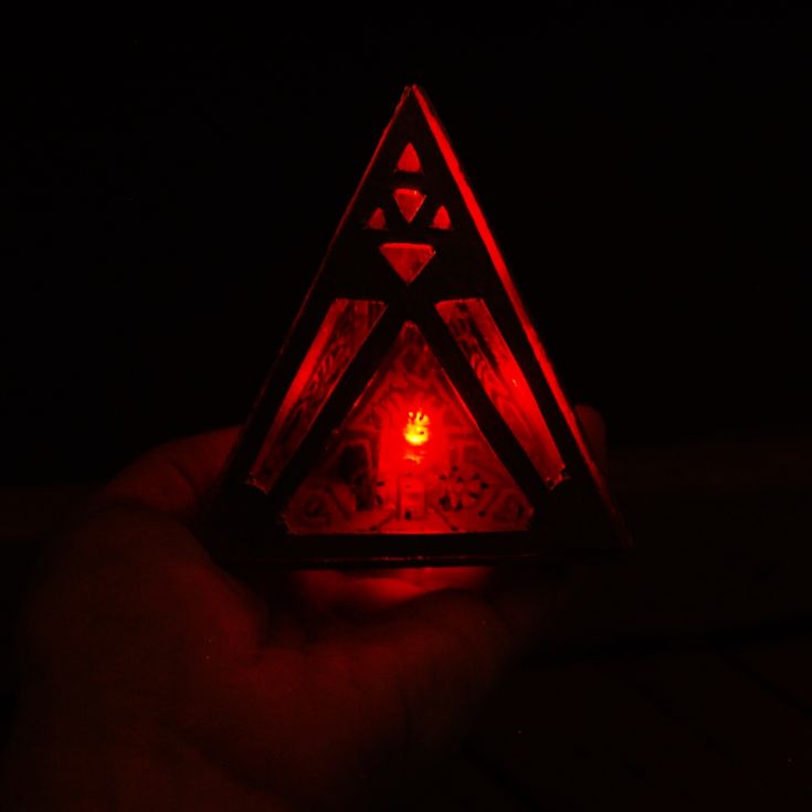 a hand holding a triangle shaped object with red light in it's center and two triangles on the other side