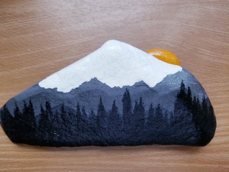 a painted rock sitting on top of a wooden table next to an orange and some trees