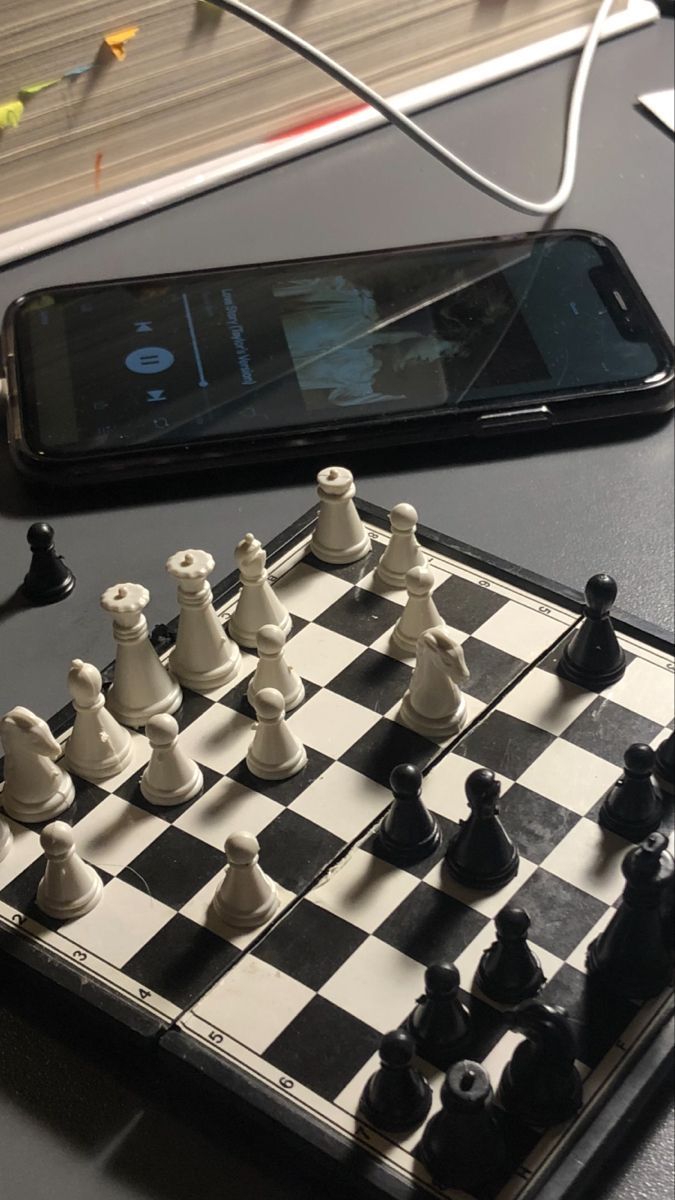 a cell phone sitting on top of a table next to a chess board and pieces