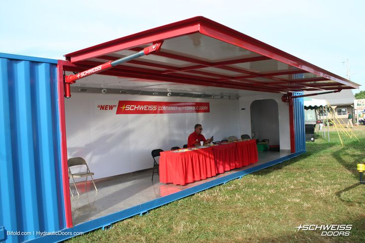 a man sitting at a table inside of a blue and red shipping container on the grass