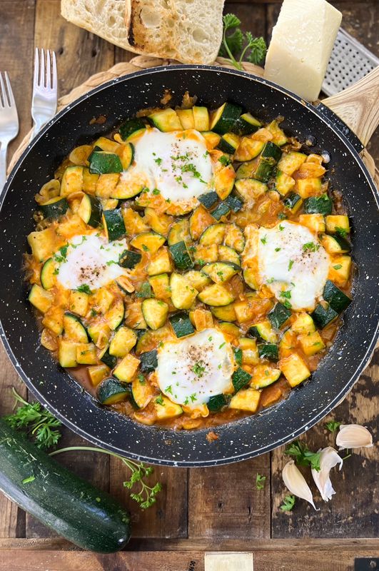 an iron skillet with eggs and zucchini in it on a wooden table