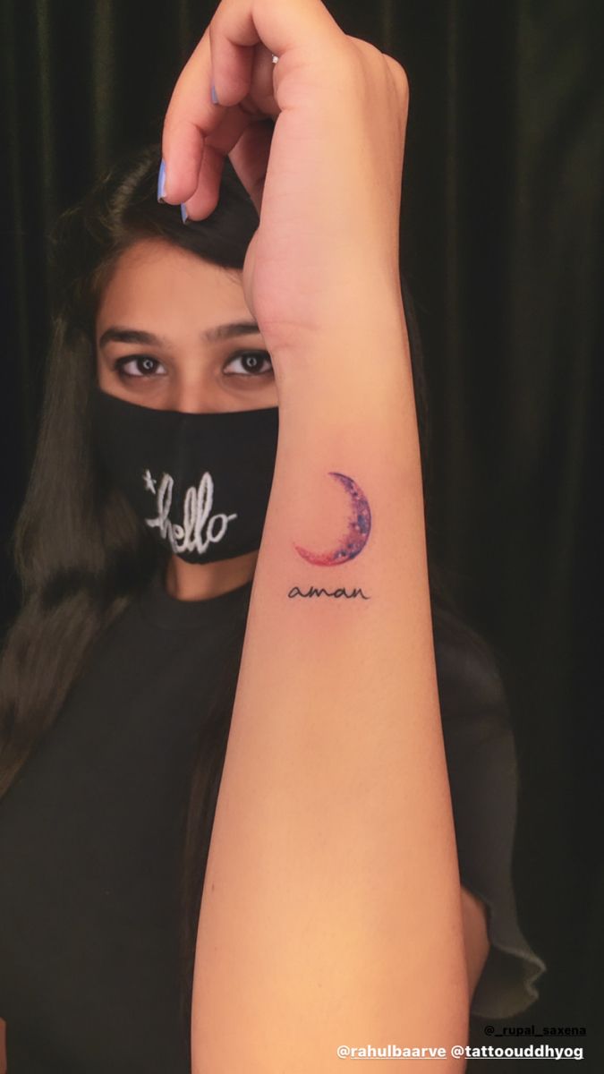 a woman wearing a black face mask with the word hello written on it and a crescent tattoo behind her arm