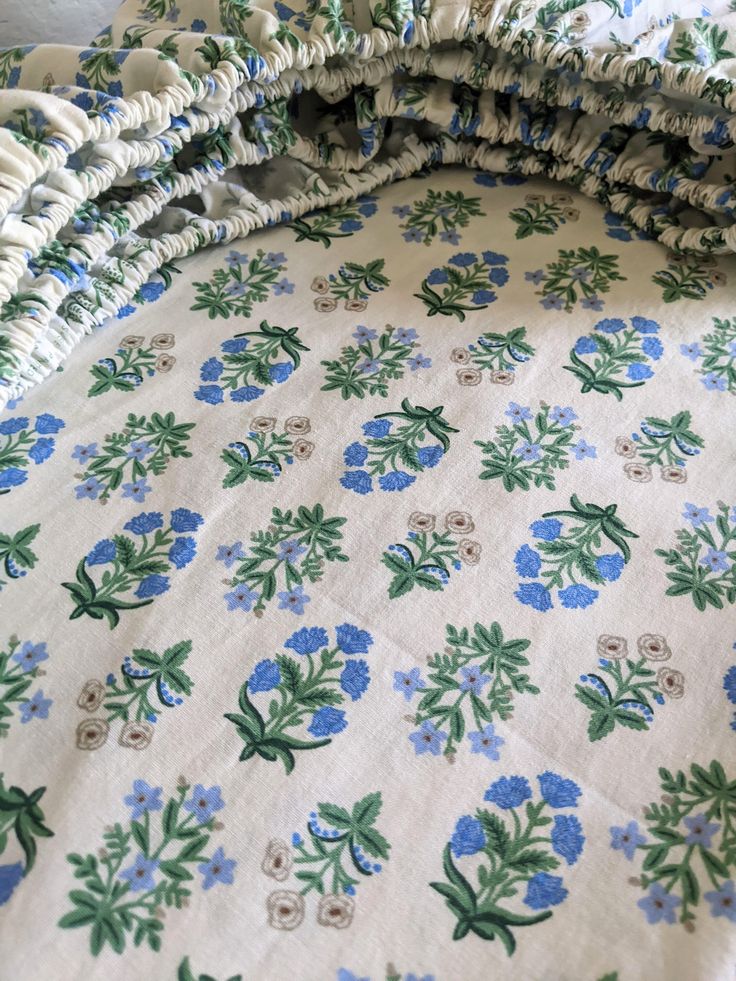 an unmade bed with blue and green flowers on it