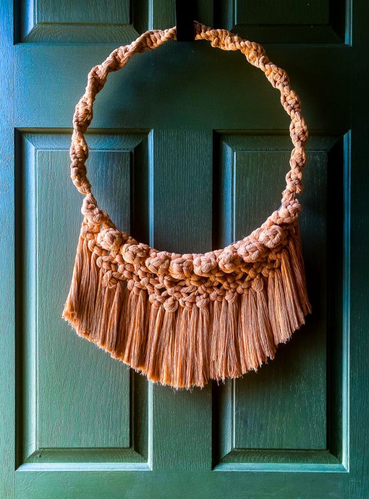 a tasseled necklace hanging on a green door with a wooden frame in the shape of a circle