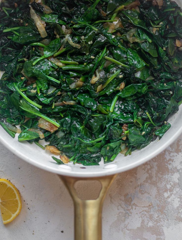 a white bowl filled with spinach and other vegetables on top of a table next to an orange slice