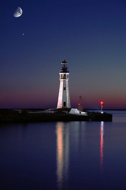 a light house sitting on top of a body of water at night with the moon in the sky