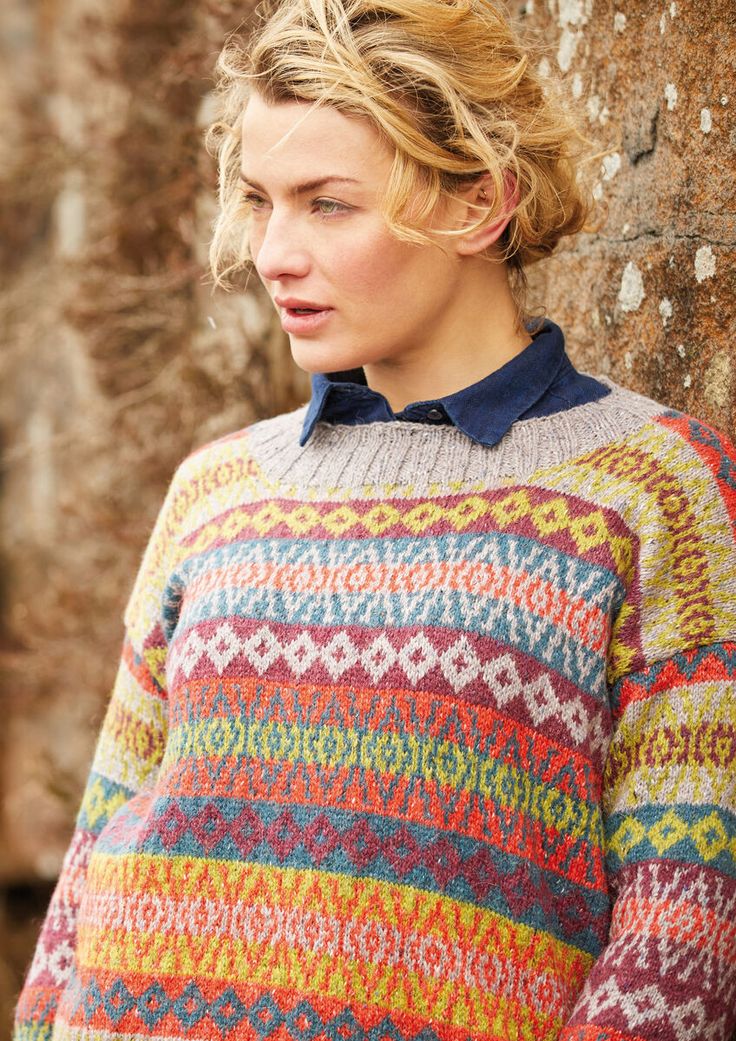 a woman standing next to a tree wearing a colorful sweater