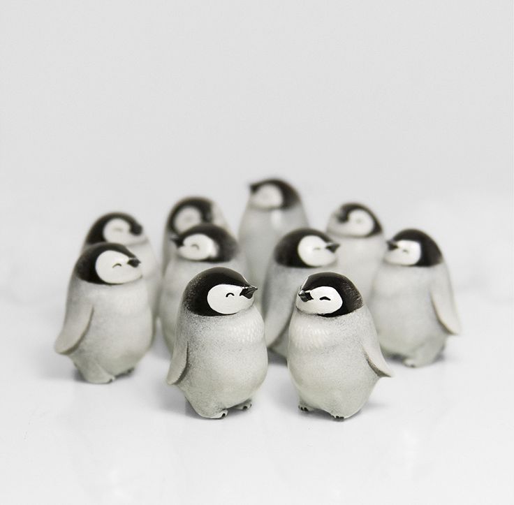 a group of small penguins standing next to each other on a white surface with one penguin looking at the camera