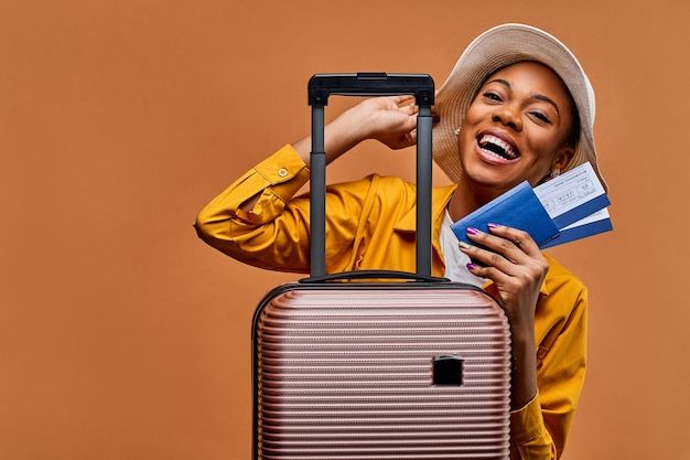 a woman with a hat and yellow jacket is holding a piece of luggage in front of her face