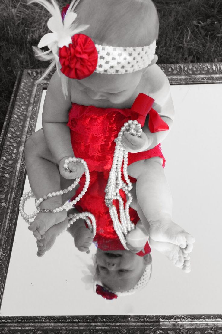 a baby girl wearing a red and white outfit with pearls on it's head