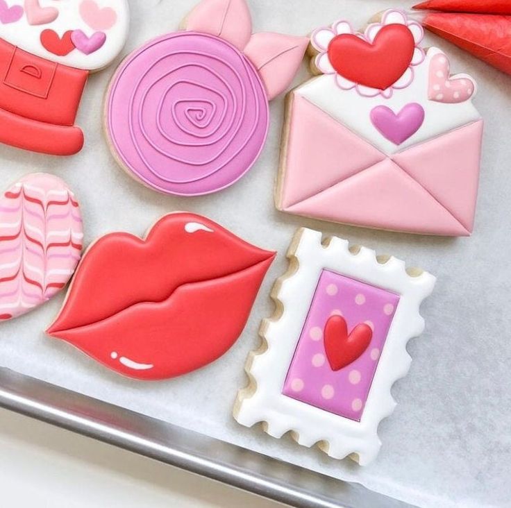 decorated cookies are displayed on a tray with pink and red decorations in the shape of envelopes