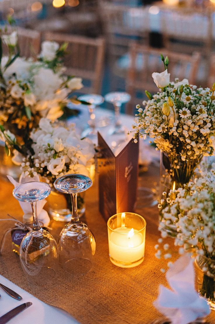 a table topped with vases filled with white flowers and candles next to each other