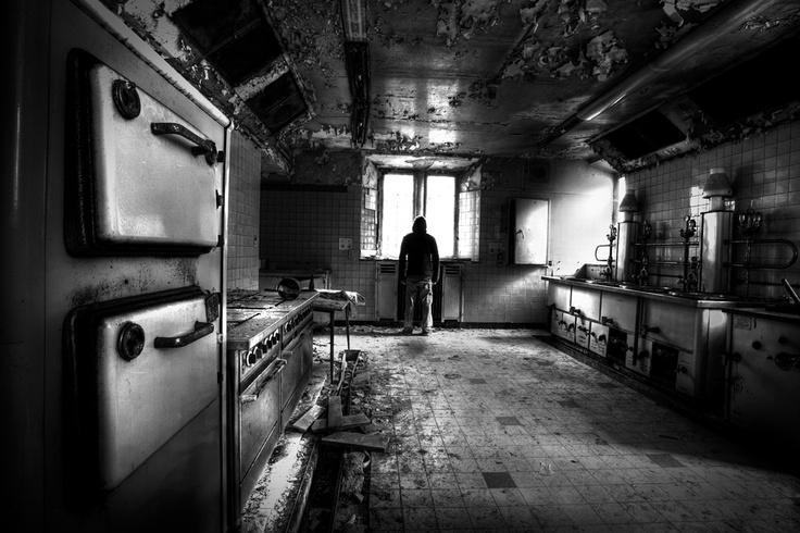 a black and white photo of a man standing in an old, run down kitchen