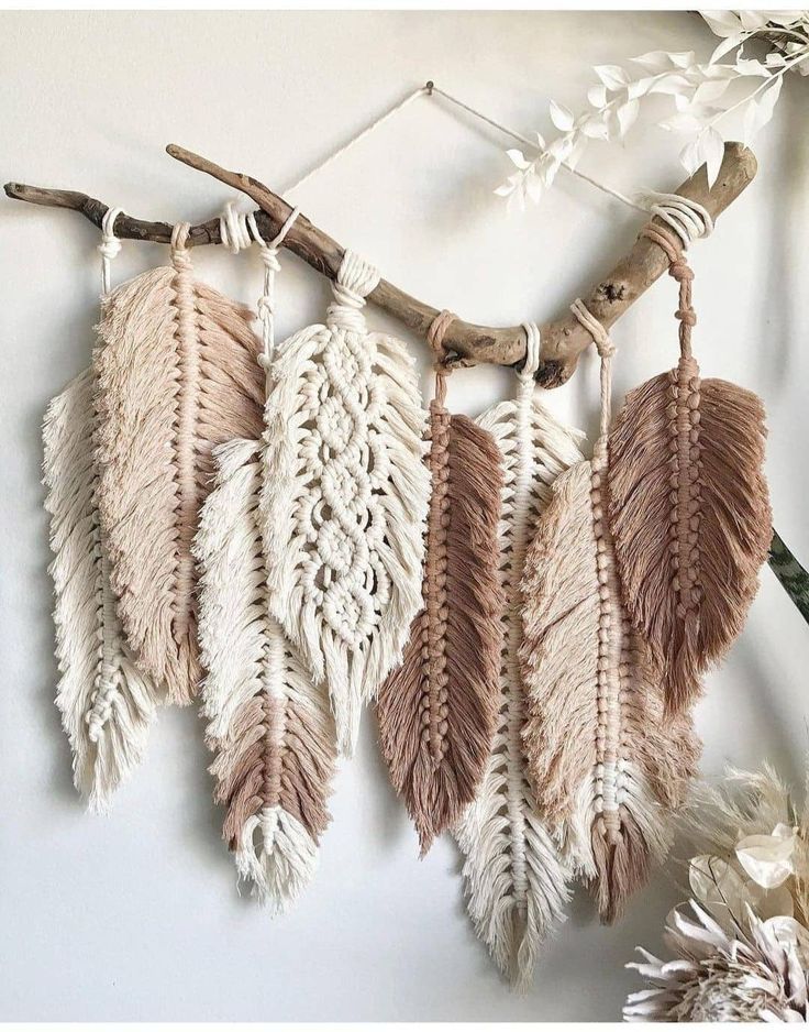 a group of feathers hanging from a branch on a wall next to flowers and branches