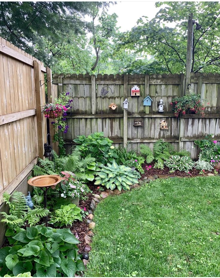 a backyard garden with lots of plants and flowers in the back yard, along with a wooden fence