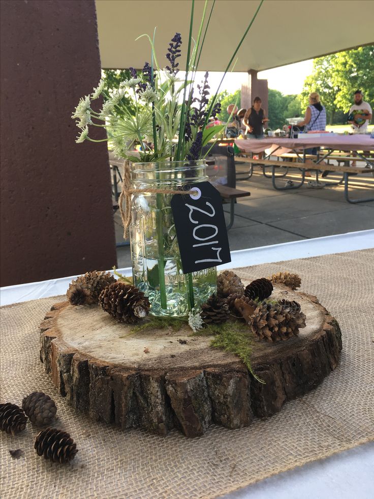 a glass vase filled with flowers sitting on top of a wooden stump next to pine cones