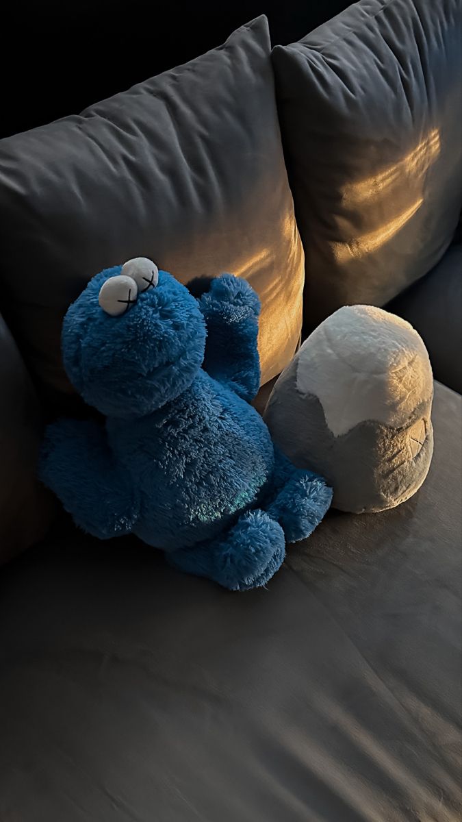 a blue teddy bear sitting on top of a couch next to a white ball and pillow