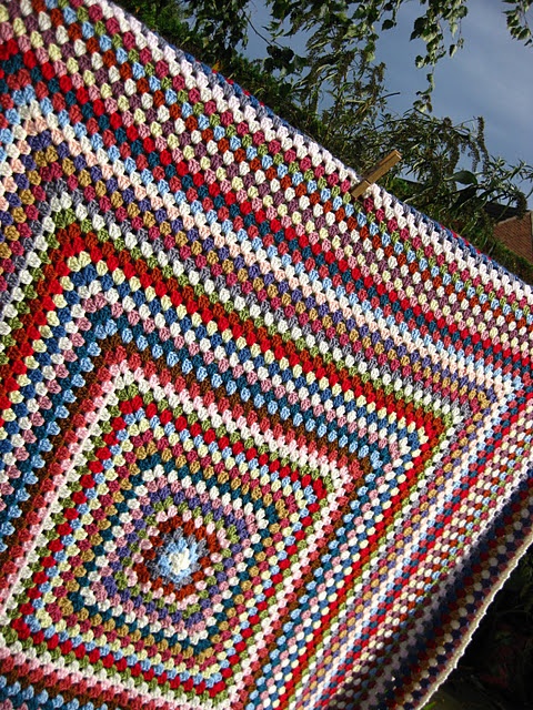 a crocheted blanket is hanging outside on a clothes line with trees in the background