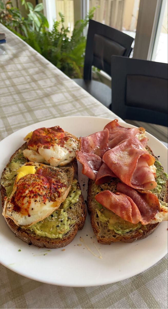 an open face sandwich with eggs, bacon and avocado on it sitting on a white plate