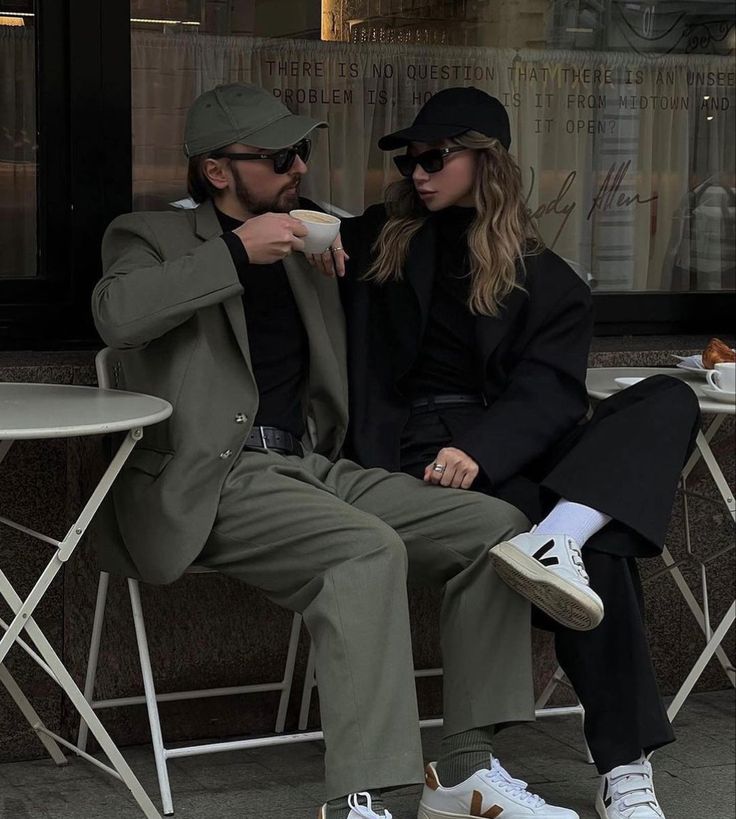 a man and woman sitting next to each other in front of a building drinking coffee