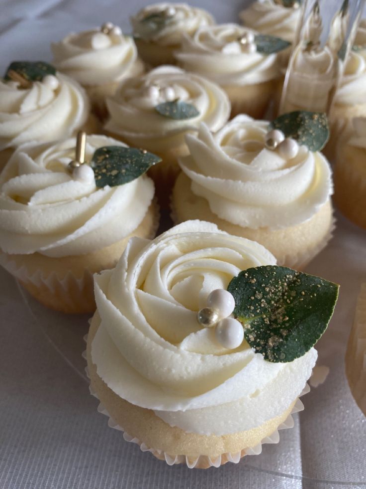 cupcakes with white frosting and green leaves are on a tablecloth, ready to be eaten