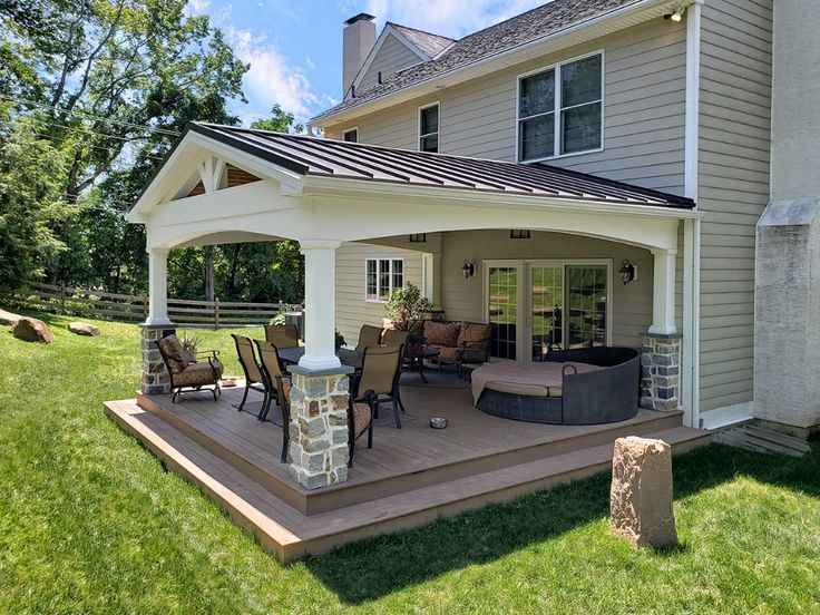 a covered patio with chairs and table in front of a house