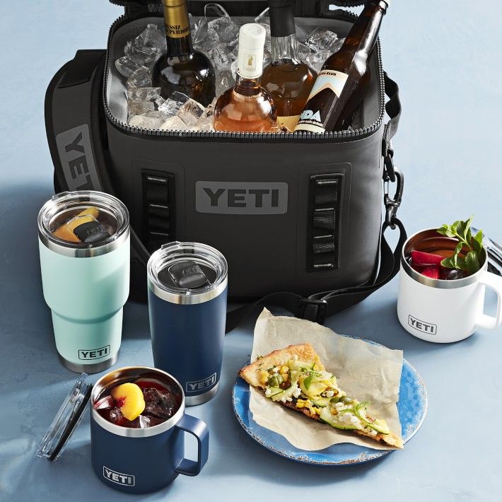 a cooler filled with drinks and food on top of a blue tablecloth next to two mugs