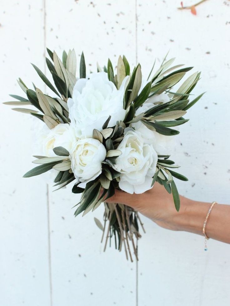 a bouquet of white flowers is held by a woman's hand against a wall