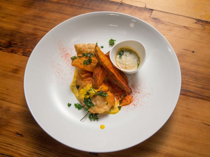 a white plate topped with food and sauce on top of a wooden table next to a cup