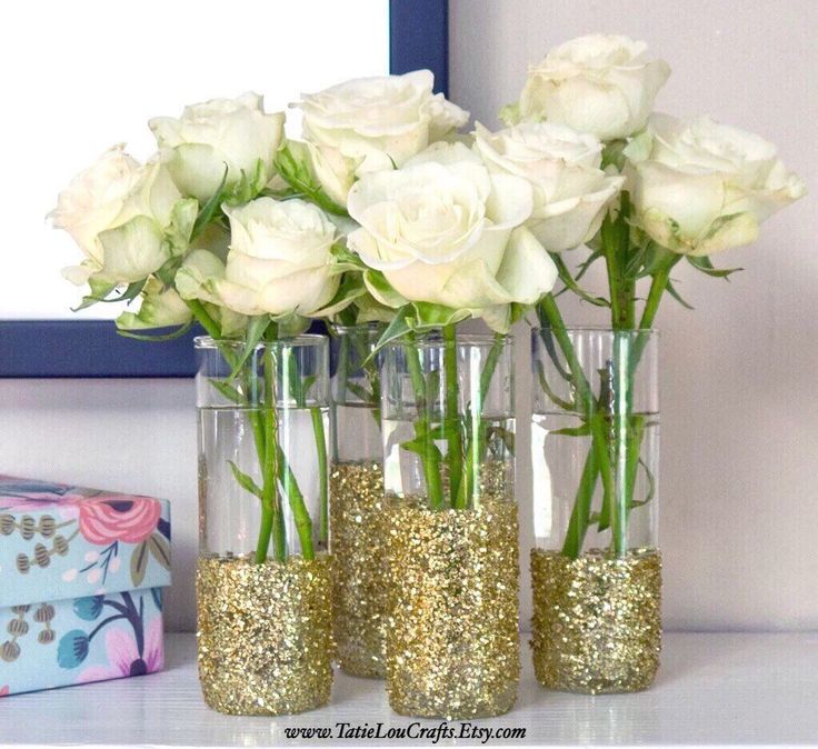 three vases filled with white roses and gold glitter