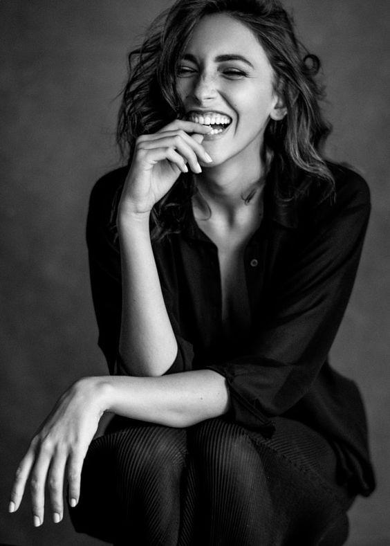 a black and white photo of a woman smiling with her hands on her chins