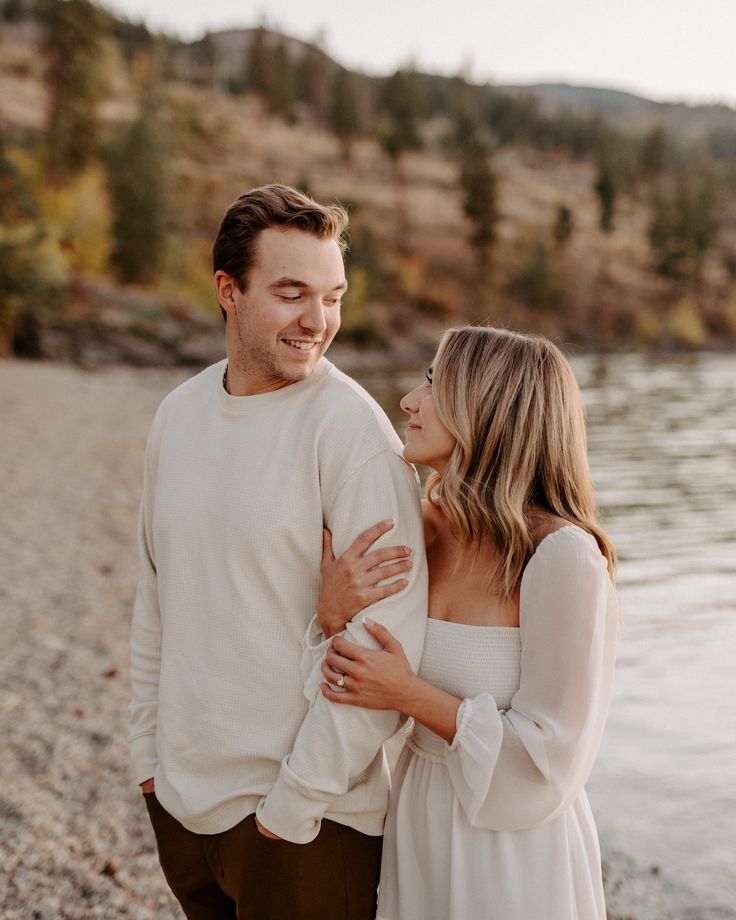 a man and woman standing next to each other on the shore of a body of water