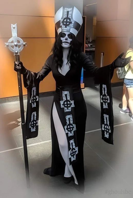 a woman dressed as a skeleton holding two scepts and wearing a long black dress