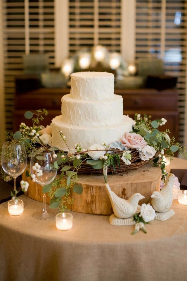 a white wedding cake sitting on top of a wooden table next to candles and flowers