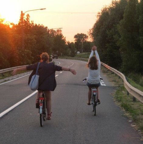 two people riding bikes down the road with their arms in the air as the sun sets