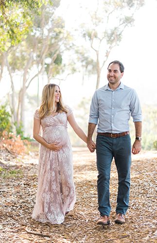 a pregnant couple holding hands and walking through the woods