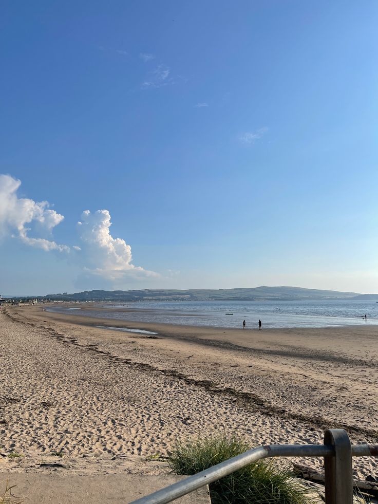 people are walking on the beach near the water and sand, with blue skies in the background