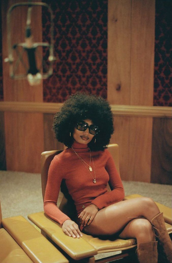 a woman sitting in a chair with an afro haircut and glasses on her face