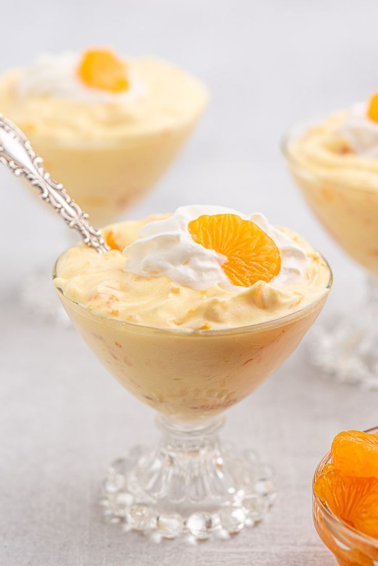 three desserts with orange slices and whipped cream in small glass bowls on a table